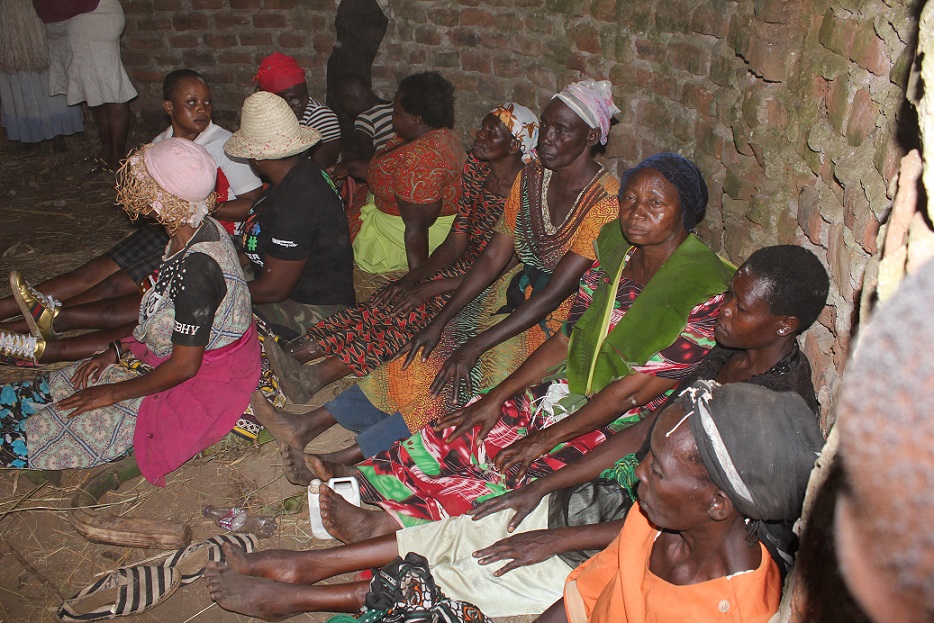 The female relations of Khabeli Watuwa and Gidudu sitting legs stretched waiting for the successful completion of the circumcision
